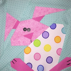 May include: A pink bunny rabbit with a white and colorful polka dot egg. The bunny has black button eyes and a pink nose.
