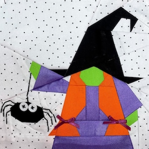 May include: A purple and orange witch with a black hat and a green face. The witch is holding a black spider with white buttons for eyes. The background is white with black polka dots.
