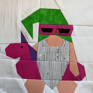 May include: A green and white gnome wearing pink sunglasses and a striped swimsuit, holding a pink inflatable flamingo.