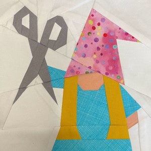 May include: A patchwork quilt block featuring a gnome with a pink and white polka dot hat, a yellow waistcoat, and a blue dress. A pair of grey scissors is also included in the block.