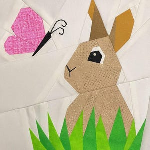 May include: A brown bunny with a pink nose and black eyes is sitting in green grass. A pink butterfly with black markings is flying above the bunny.