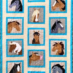 May include: A beige quilt with a turquoise border features a patchwork design of horse heads. The quilt is decorated with the words "Hay Girl" and "Haavaay".