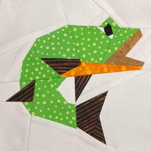 May include: A green, brown, and orange patchwork fish with white polka dots. The fish is made of fabric and is a quilt block.