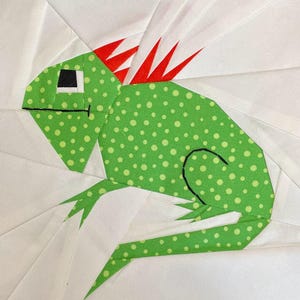 Puede incluir: Iguana de tela verde con púas rojas de tela en la espalda. La iguana está hecha de tela verde con lunares blancos y tiene detalles bordados negros.