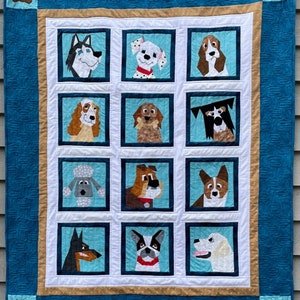 May include: A blue and tan quilt with a white background featuring 12 different dog breeds in individual squares. Each dog is depicted in a cartoon style with a simple, colorful design.