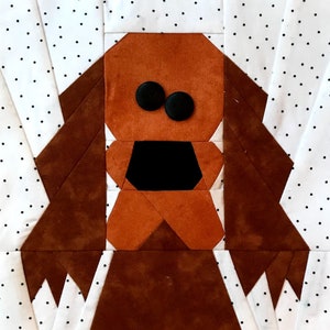 May include: A brown fabric dog with black button eyes and a black fabric nose. The dog is made of fabric squares sewn together in a geometric pattern. The dog is on a white background with black polka dots.