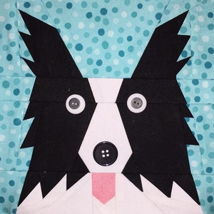 May include: A black and white patchwork dog face with a pink tongue, black button eyes, and a black button nose. The dog is on a blue background with white polka dots.