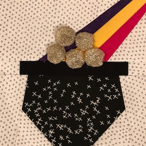 May include: A black fabric pot with a white plus sign pattern, filled with gold glitter balls. The pot is on a white background with a black and white polka dot pattern.