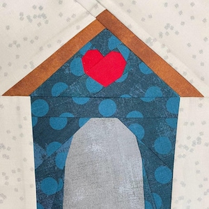 May include: A blue and white patterned fabric house with a red heart on the roof. The house is made of fabric and has a brown roof.