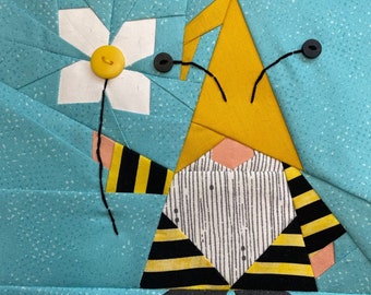 Puede incluir: Un gnomo con rayas amarillas y negras, con un sombrero amarillo y una flor blanca con un centro amarillo. El gnomo tiene ojos negros y una cara rosa.