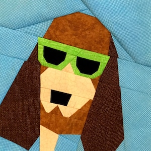 May include: A brown and white dog wearing green sunglasses. The dog's ears are brown and the background is blue.