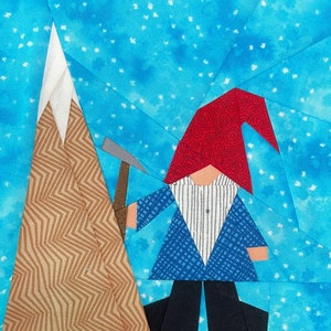 Peut inclure: Une œuvre d'art textile fantaisiste représentant un gnome avec un chapeau rouge et une veste bleue, tenant une pioche. Une montagne avec un sommet blanc est à gauche. Le fond est bleu clair avec des mouchetures blanches, créant un effet de neige. Le gnome est devant la montagne.