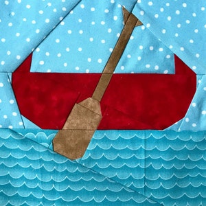 May include: A fabric quilt block featuring a red boat centered on a light blue background with white polka dots. A brown paddle is positioned diagonally across the boat. The bottom section depicts stylized blue waves with white curved lines.