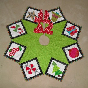 Puede incluir: Una falda de árbol de Navidad verde con un borde negro y blanco. La falda tiene ocho paneles, cada uno con un diseño diferente con temática navideña, que incluye una estrella, una media, un bastón de caramelo, un regalo, un lazo, un árbol y un adorno.
