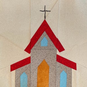 May include: A red and gray church with a cross on top. The church has a red roof with a swirl pattern and a gray body with a brown door. The windows are blue.