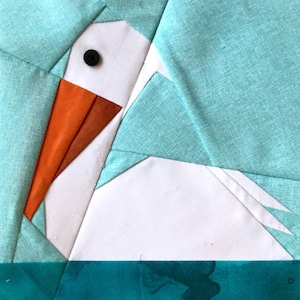 May include: A white fabric pelican with an orange beak and a black eye, sitting on a teal blue fabric background.