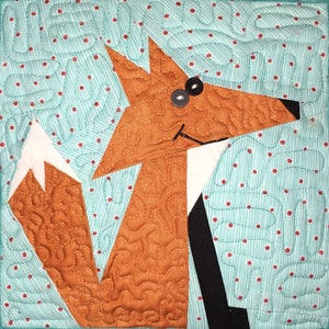 Puede incluir: Un zorro marrón con cola blanca y patas negras está aplicado sobre una tela turquesa con lunares rojos. El zorro tiene la nariz negra y dos ojos negros con pupilas grises.