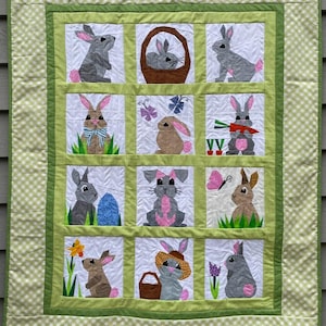 May include: A handmade Easter-themed quilt featuring nine squares with appliqued bunnies in various poses. The quilt has a green and white gingham border and a green frame around each bunny square. The bunnies are gray, brown, and pink.