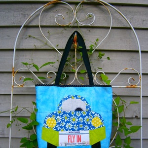 May include: A blue tote bag with a white and yellow daisy patterned car design. The car has a license plate that reads "Wisconsin Fly In".