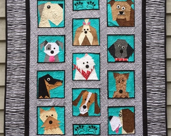 May include: A quilt with a black and white striped border and a turquoise background. The quilt features 12 different dog faces in individual frames. Each dog face is made of fabric and has a unique expression.