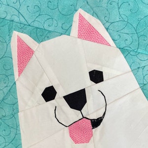 May include: A white fabric dog with pink ears and a pink tongue sticking out. The dog's eyes and nose are black.