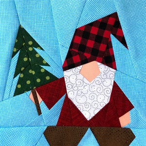 May include: A red and white plaid gnome holding a green Christmas tree with yellow polka dots. The gnome is wearing a red hat and has a white beard with a swirl pattern. The background is a light blue fabric with a grid pattern.