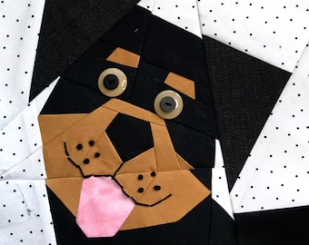 May include: A brown and black patchwork dog face with a pink tongue sticking out. The dog's eyes are made of buttons.
