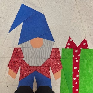 May include: A red and white polka dot gift box with a green bow is next to a gnome with a blue hat, a white beard, and a red and white polka dot shirt.