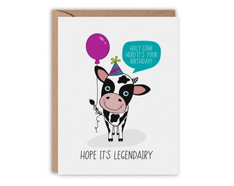 May include: A birthday card featuring a black and white cow with a purple balloon and a party hat. The card has the text "Holy Cow! Herd it's your birthday!" and "Hope it's Legendairy."