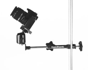 May include: A black camera mounted on a CamStand. The stand has a black base and a silver vertical pole. The camera is angled downward. The CamStand logo is visible on the horizontal arm.