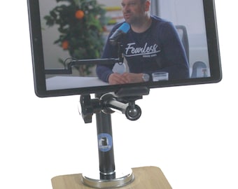May include: A black tablet stand with a flexible arm and a magnetic base. The stand is made of metal and has a black finish. The tablet is mounted on the stand and is displaying a video of a man talking. The man is wearing a blue shirt with the word "Fearless" printed on it.