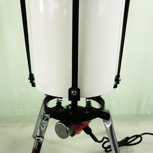 May include: A white bucket with a black metal frame and a silver stand with a red electric motor. The stand has three legs and a black base. The bucket is suspended from the frame by four metal hooks.
