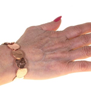 Peut inclure: Un bracelet en cuivre compos&eacute; de pi&egrave;ces de monnaie. Le bracelet est fait de pi&egrave;ces de monnaie li&eacute;es, affichant les faces et les piles des pi&egrave;ces. Le bracelet est port&eacute; au poignet, avec la main et les doigts visibles. Les ongles sont peints en rose vif.