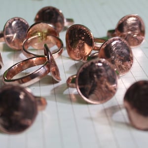 May include: A collection of copper rings, each featuring a unique design. The rings are made from repurposed coins and have a rustic, vintage aesthetic.
