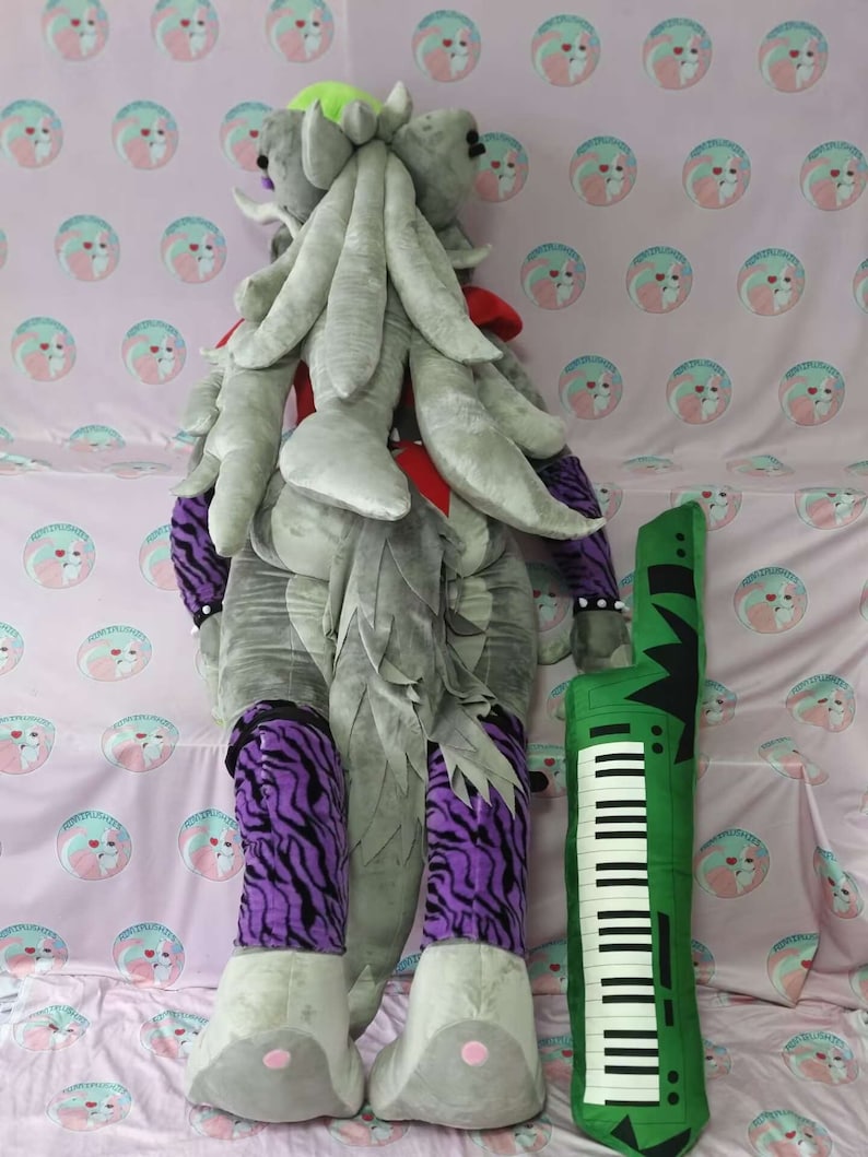 May include: A gray and purple plush toy with a long gray tail and a green keyboard. The toy is wearing a red and black vest and has a green mohawk.