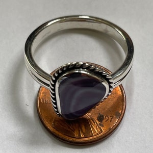 May include: A silver ring with a purple and white agate stone set in a silver bezel. The ring is shown next to a US penny for size comparison.