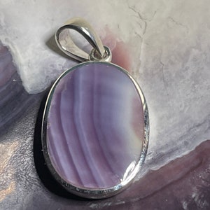 May include: A silver pendant with a purple and white agate stone. The stone is oval shaped and has a swirling pattern.