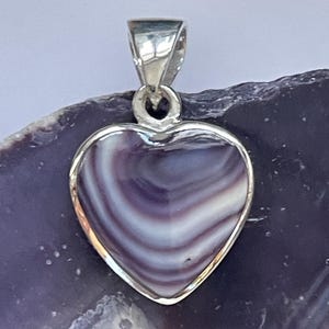 May include: A silver heart-shaped pendant with a purple and white shell inlay. The pendant is on a white background.