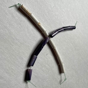 May include: Two strands of beads, one white with brown swirls and one purple with white swirls. The beads are cylindrical and have a smooth, polished finish.