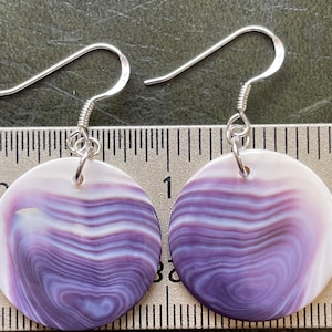 May include: A pair of silver earrings with purple and white shell round pendants. The earrings are approximately 1 inch in diameter.