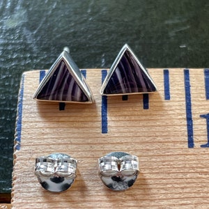May include: A pair of silver triangle earrings with purple and white striped stone accents. The earrings have a post back.