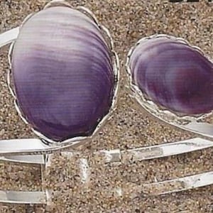 May include: A silver bracelet with two purple shell accents. The bracelet is double-banded and has a delicate, ornate design.