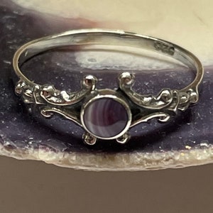 May include: A silver ring with a purple and white stone set in a decorative design.