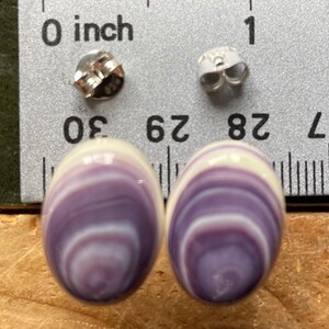 May include: A pair of oval-shaped earrings made from purple and white seashells. The earrings are approximately 0.75 inches in length and are set in silver.