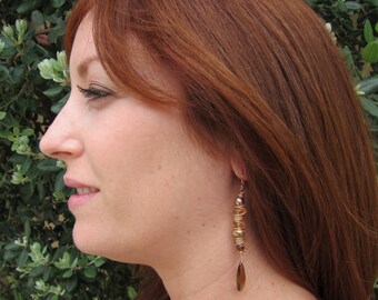 May include: A woman with long, auburn hair wearing a pair of gold dangle earrings with brown and gold beads and a leaf-shaped charm.