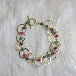May include: Gold bracelet with a chain of interlocking circles and colorful beads. The beads are blue, green, and pink.