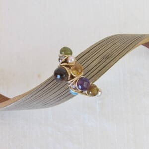 May include: A gold wire wrapped bracelet with a cluster of colorful gemstones, including amethyst, citrine, and green stones.