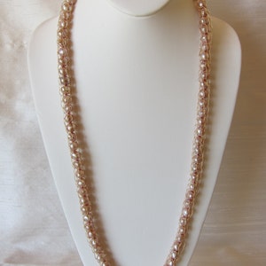 May include: A long necklace made of pale pink pearls strung on a gold wire. The necklace is displayed on a white mannequin.