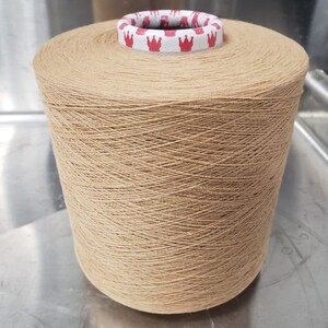 Può includere: Un rocchetto di filo beige con un'etichetta bianca con corone rosse.