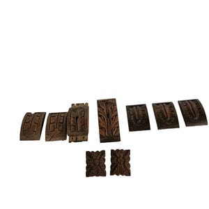 May include: A collection of intricately carved wooden decorative elements. The pieces vary in shape and size, featuring floral and geometric patterns. The wood has a rich, dark brown color, suggesting age and craftsmanship. Ideal for woodworking projects or home decor.